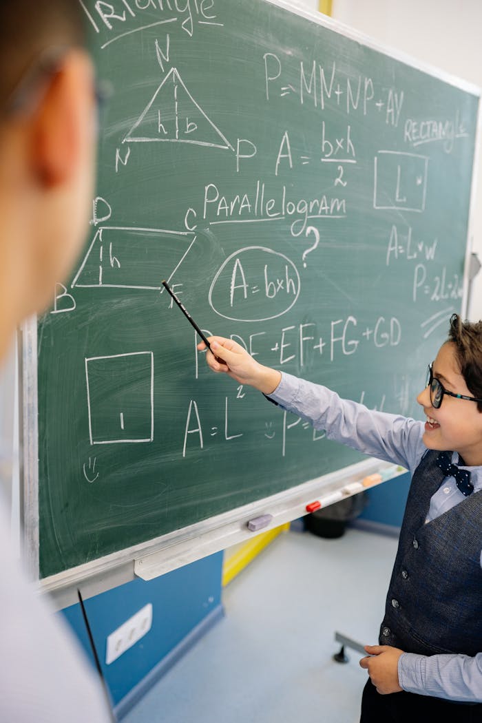 A boy confidently presents mathematical formulas on a chalkboard in class, illustrating geometry concepts.