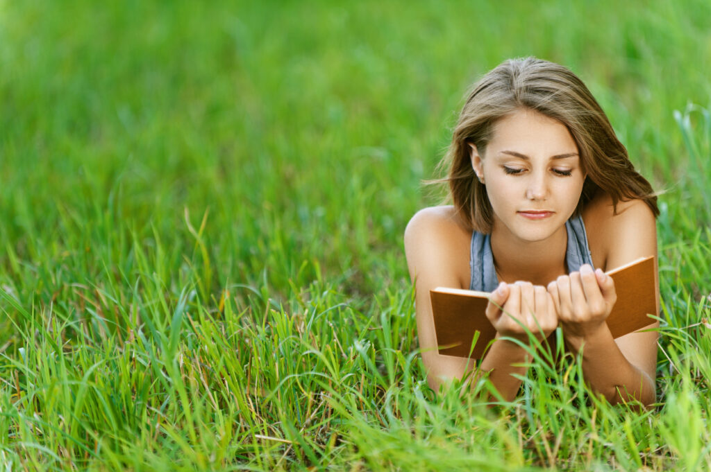 Cours particuliers young woman student reading book on grass